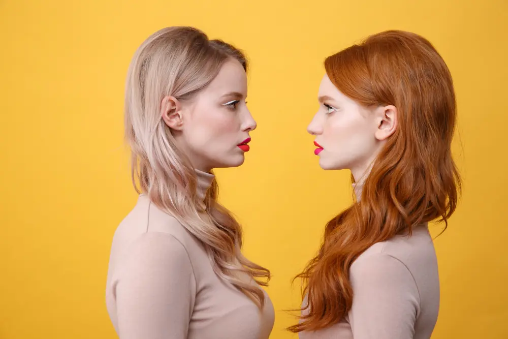 Two female creators with bright makeup facing off in a Fansly vs OnlyFans comparison.