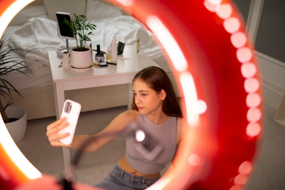 OnlyFans creator in a bedroom studio using a ring light and smartphone to take photos for her UK OnlyFans business.