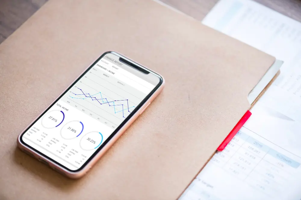 Smartphone with financial analytics graphs on a document folder for UK OnlyFans creator tax filing.
